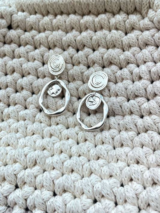 Némésis – Boucles d’Oreilles Argentées Spirales & Pièces Antiques
Puissantes. Mystiques. Éternelles.
Les boucles Némésis tirent leur nom de la déesse grecque de la justice et de l’équilibre. Fusion parfaite entre héritage antique et design symbolique, elles arborent des spirales élégantes et des médaillons inspirés des pièces antiques, où se dessinent les silhouettes d’Athéna la sage et de Pégase, le messager ailé.